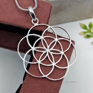May include: A silver-toned pendant featuring a geometric pattern of overlapping circles arranged in a flower-like design. The pendant is suspended from a silver-toned chain and includes the text SilverGoldWorks printed in the lower right corner.