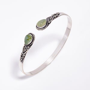 May include: Open cuff bracelet with two oval, light green gemstones. The silver-toned metal bracelet features ornate detailing around the gemstones and on the ends. The bracelet is designed to be worn on the wrist.