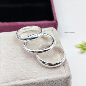 Könnte beinhalten: Drei polierte Silberringe mit einem glatten, abgerundeten Banddesign. Die Ringe sind in einer überlappenden Formation angeordnet. Der Text SilverGoldWorks ist in der oberen rechten Ecke des Bildes sichtbar. Die Ringe haben eine glänzende Oberfläche.