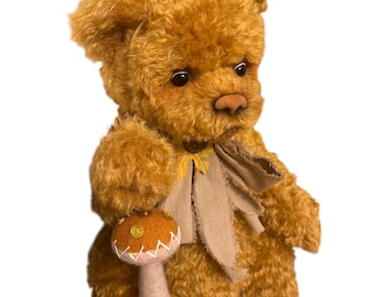 May include: A handmade, golden-brown teddy bear wearing a party hat and holding a mushroom toy. The bear has a bow tie and is holding the mushroom. The hat is tan with gold detailing. The bear is a plush toy.