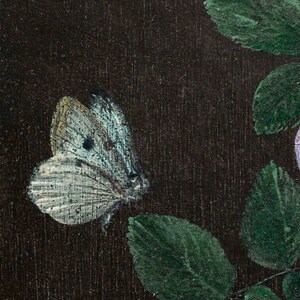 May include: A white butterfly with black spots on its wings is perched on a green leaf. The butterfly is painted on a dark brown background.