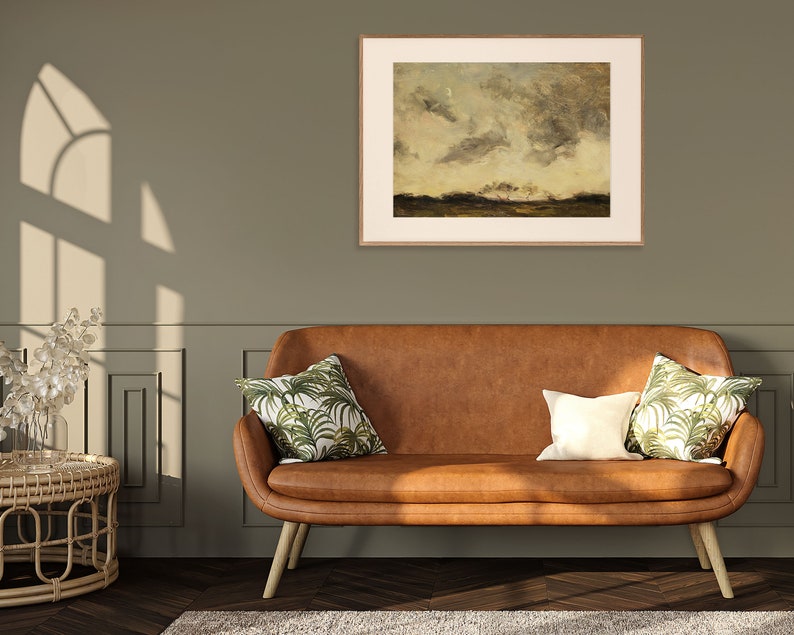 May include: A brown leather sofa with two throw pillows featuring a tropical leaf pattern. The sofa is in front of a green wall with a framed landscape painting above it.