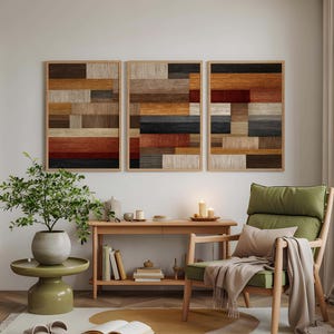 May include: A cozy living room scene featuring three framed abstract art pieces with a geometric design in shades of brown, red, and black. A green armchair with a beige throw and pillow sits near a wooden side table. A round rug and a small green side table with a plant complete the scene.