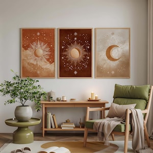 May include: Three framed celestial art prints featuring sun and moon designs in warm earth tones. The artwork hangs above a wooden console table and a green armchair with a blanket. A small side table with a potted plant and a rug complete the cozy interior.
