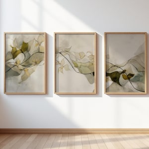 Op de afbeelding: Drie ingelijste kunstdrukken met abstracte botanische ontwerpen. Elke print heeft een lichte achtergrond met vloeiende lijnen en bladeren in aquarel-stijl in groen- en geeltinten. De frames zijn gemaakt van lichtgekleurd hout.