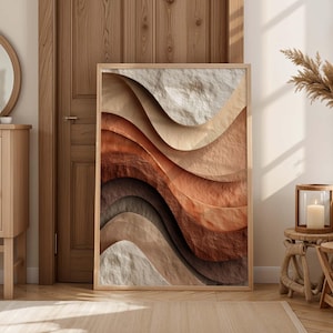 May include: A framed abstract art print with layered, textured waves in beige, brown, and rust hues. The artwork is presented in a light wood frame, creating a warm, earthy aesthetic. The print is leaning against a wooden door.
