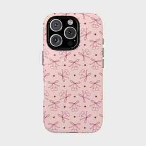 Op de afbeelding: Een roze telefoonhoesje met een herhaald patroon van rode kersen vastgebonden met strikken en kleine rode hartjes. De hoes heeft een camera-uitsparing en zwarte zijknoppen.