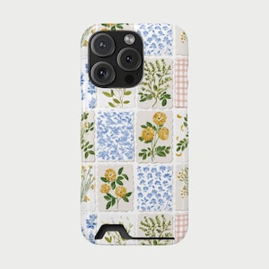 Op de afbeelding: Een witte telefoonhoes met een bloemenpatchworkontwerp. De hoes heeft een raster van kleine vierkanten, elk met een andere bloemenillustratie in tinten geel, blauw en groen. Een gedeelte van roze ruitjesstof bevindt zich aan de rechterkant.