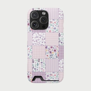 Op de afbeelding: Een telefoonhoesje met een patchwork-ontwerp met bloemen- en geometrische patronen in tinten paars, roze en wit. De hoes heeft een camera-uitsparing en een ingebouwde standaard.