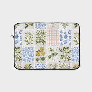 Op de afbeelding: Een rechthoes voor een laptop met een bloemenpatroon. Het ontwerp heeft een patchwork van botanische illustraties, waaronder gele en blauwe bloemen, en een roze ruit. De hoes heeft een zwarte ritssluiting.