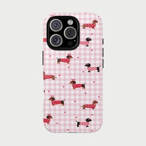 Op de afbeelding: Een telefoonhoesje met een roze en wit geruit patroon. De hoes heeft een herhalend patroon van teckel honden die truien dragen met hartaccenten. Kleine rode hartjes zijn verspreid over de achtergrond.