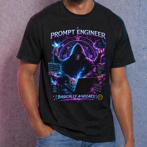 May include: Black t-shirt with a graphic design. The design features the text "PROMPT ENGINEER" above an illustration of a person in a hoodie using a laptop. The design includes purple and blue accents and the phrase "(BASICALLY A WIZARD)".