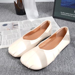 May include: A pair of off-white, square-toe ballet flats. The shoes have a smooth, leather-like appearance with a light brown interior. The flats are displayed on a newspaper, suggesting a casual, everyday style.