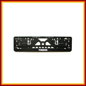 May include: A black rectangular plastic number plate holder featuring a complex structural frame with multiple mounting slots and holes. The word Mazda is printed in white, sans-serif capital letters centred along the bottom edge of the frame.