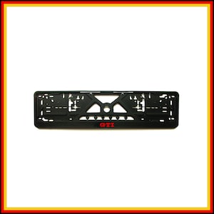 Puede incluir: Un soporte rectangular negro para matrícula con un diseño geométrico recortado y el texto rojo GTI impreso en la parte inferior central. El marco incluye múltiples ranuras y orificios de montaje para una fijación segura al parachoques.