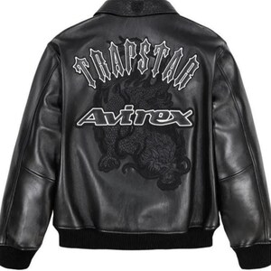 May include: Black leather jacket with a ribbed collar and cuffs. The back features the text "TRAPSTAR" above the word "Avirex" and a detailed dragon graphic. The jacket has a classic bomber style.