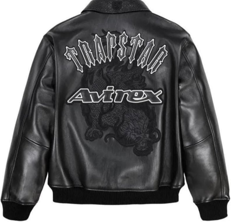 May include: Black leather jacket with a ribbed collar and cuffs. The back features the text "TRAPSTAR" above the word "Avirex" and a detailed dragon graphic. The jacket has a classic bomber style.