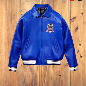 May include: A vibrant blue leather jacket with a white and black striped trim on the cuffs and hem. The jacket features a front zipper and a patch on the chest with a crest design. The jacket has a classic bomber style.