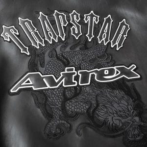 May include: Black leather jacket with white embroidered text that reads "TRAPSTAR" above "Avirex". A detailed dragon design is embroidered below the text, adding a bold, edgy aesthetic. The jacket's design is suitable for streetwear.