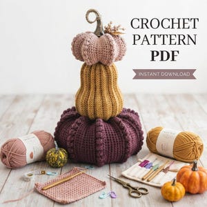 May include: A stack of three crocheted pumpkins in dusty pink, mustard yellow, and deep plum, accompanied by yarn skeins, a crochet hook set, scissors, a measuring tape, and small real pumpkins. Text reads: CROCHET PATTERN PDF INSTANT DOWNLOAD.