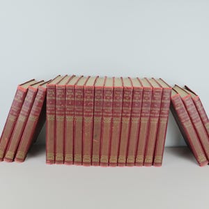 May include: A collection of seventeen matching hardcover books with deep red spines and gold-colored lettering. The books are arranged in a row, with the central group standing upright and the end books leaning inward toward the center of the set.