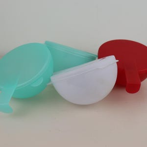 May include: A collection of colorful plastic containers. The containers are in various colors, including teal, white, and red. Each container has a rounded shape with a handle-like extension. The objects are likely for food storage.