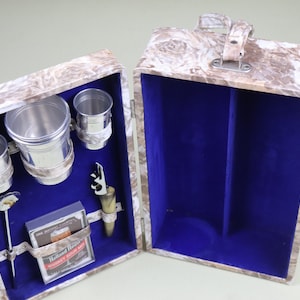 May include: A brown and white patterned travel bar set with a blue velvet interior. The set includes four silver cups, a bottle opener, a stirrer, and a pack of Holland House Whiskey Sour Mix.