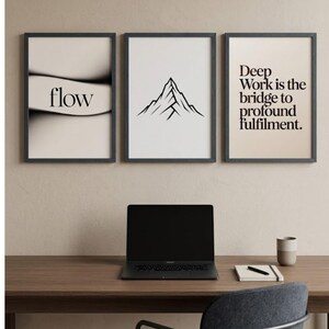 May include: Three framed art prints with motivational text and minimalist designs. One print says "flow", another features a mountain outline, and the third reads "Deep Work is the bridge to profound fulfillment." A laptop, notebook, and mug sit on a wooden desk.