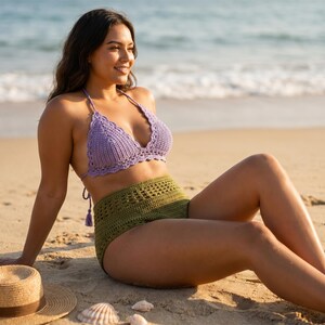 May include: A lavender crochet bikini top and olive green high-waisted crochet shorts. The beachwear is handmade with a textured stitch pattern. A straw hat and seashells are in the sand.
