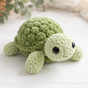 May include: A handmade, plush green turtle with a textured shell and soft, rounded features. The turtle has large, black eyes and a smiling expression, perfect for a child's toy or nursery decor.