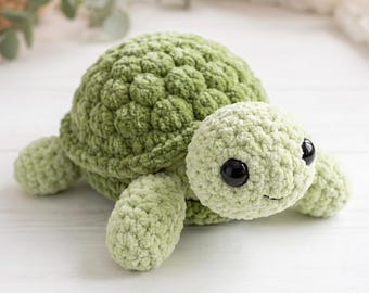 May include: A handmade, plush green turtle with a textured shell and soft, rounded features. The turtle has large, black eyes and a smiling expression, perfect for a child's toy or nursery decor.