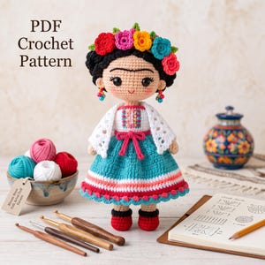 May include: A crochet doll with black hair, a colorful floral crown, and dangling earrings. The doll wears a white top with embroidery, a teal skirt with pink and white stripes, and red shoes. Text reads: PDF Crochet Pattern. Bloom-Brow Artist Doll Pattern.