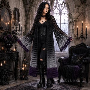 May include: A long, open-front crochet cardigan featuring a gradient colour pattern that transitions from black at the shoulders to grey and ends in a deep purple hem. The garment has wide, flared sleeves and is worn over a black corset top and ripped jeans.