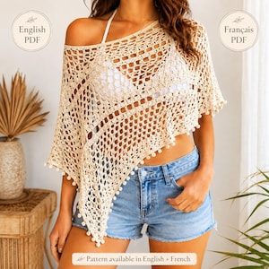 Könnte beinhalten: Ein beigefarbener Häkelponcho mit durchbrochenem Rautenmuster und einem gewellten Saum mit kleinen Bommel-Akzenten. Das Kleidungsstück wird über einem weißen Oberteil und blauen Jeansshorts getragen. Text auf dem Bild: English PDF, Français PDF.