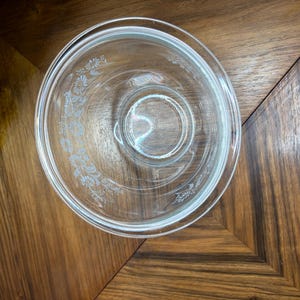 May include: A clear glass mixing bowl featuring a delicate white floral pattern etched along the interior rim. The bowl has a circular base and a wide, open top, showcasing a transparent design that allows for a clear view through the glass.