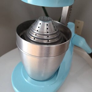 Puede incluir: Un exprimidor de c&iacute;tricos vintage azul y plateado con un colador de metal. El exprimidor tiene una palanca para presionar la fruta y un pico para verter el jugo.