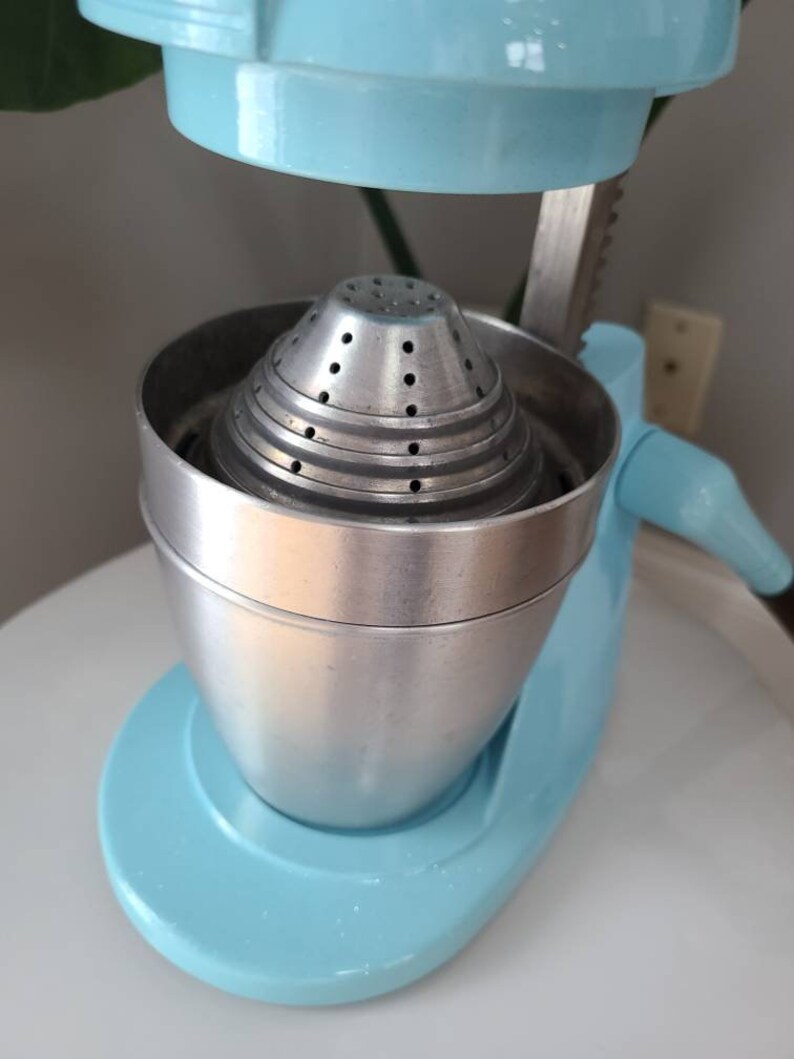 Puede incluir: Un exprimidor de c&iacute;tricos vintage azul y plateado con un colador de metal. El exprimidor tiene una palanca para presionar la fruta y un pico para verter el jugo.