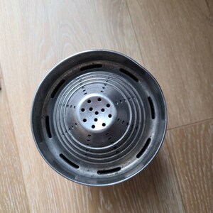 Puede incluir: Un exprimidor de c&iacute;tricos de metal plateado con una base redonda y un colador c&oacute;nico con m&uacute;ltiples agujeros.