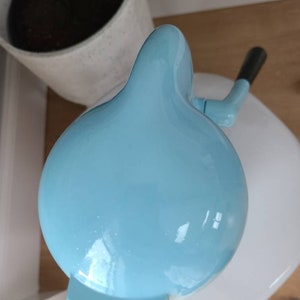 Puede incluir: Una m&aacute;quina de hacer helados de color azul claro con una base blanca y un asa. La m&aacute;quina de hacer helados tiene forma de c&uacute;pula y un acabado liso y brillante.