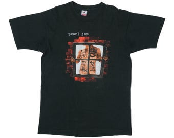 May include: A black short-sleeve t-shirt featuring the text pearl jam in white letters above a graphic of a window frame held by a torso with black ink writing on the skin, set against a red brick background pattern on the front of the shirt.