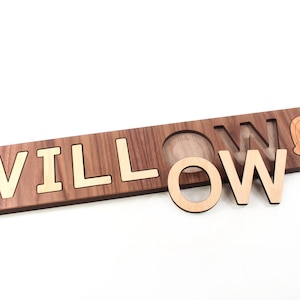 May include: Wooden puzzle with the name "WILLOW" spelled out in gold letters. The letters are removable and can be placed in the corresponding cutouts. A small rainbow cutout is also included.