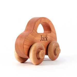 Pode incluir: Um carro de brinquedo de madeira com acabamento natural. O carro tem uma carroceria arredondada, uma al&ccedil;a e quatro rodas de madeira. O nome "Jack" est&aacute; gravado na lateral. Brinquedo para crian&ccedil;as.