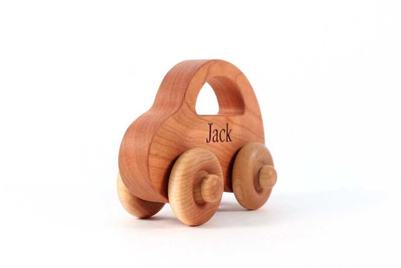 Pode incluir: Um carro de brinquedo de madeira com acabamento natural. O carro tem uma carroceria arredondada, uma al&ccedil;a e quatro rodas de madeira. O nome "Jack" est&aacute; gravado na lateral. Brinquedo para crian&ccedil;as.