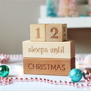 May include: Wooden countdown block set with the numbers 12, the words "sleeps until Christmas", and a pink and white garland.