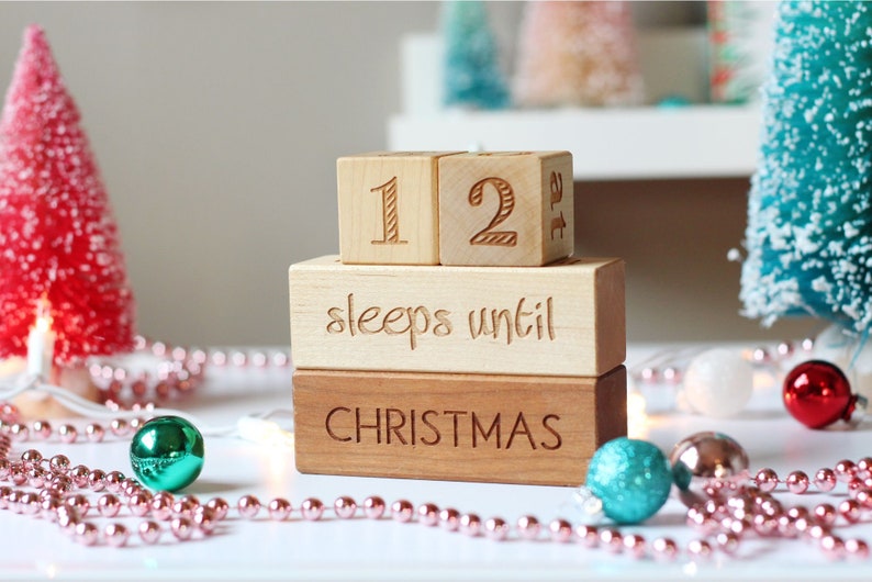 May include: Wooden countdown block set with the numbers 12, the words "sleeps until Christmas", and a pink and white garland.