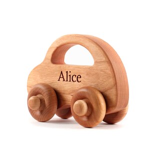 Pode incluir: Um carro de brinquedo de madeira com acabamento castanho claro. O carro tem uma carroceria arredondada com um recorte para uma al&ccedil;a e quatro rodas de madeira. O nome "Alice" est&aacute; gravado na lateral. Um brinquedo cl&aacute;ssico para crian&ccedil;as.