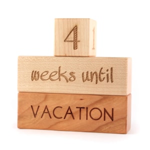 May include: Wooden blocks stacked to count down the weeks until vacation. The top block reads "4" and the middle block reads "weeks until". The bottom block reads "VACATION".