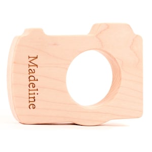 May include: A light wood camera-shaped toy with the name "Madeline" engraved on the side.