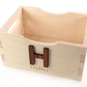 May include: A wooden storage box with a natural finish. The box has a cutout handle on the top and a wooden letter "H" on the front. The name "Halter" is engraved below the letter.