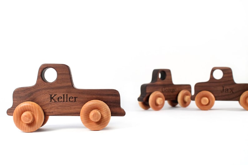 K&ouml;nnte beinhalten: Drei Holzspeilzeug-LKWs mit personalisierten Namen. Die LKWs sind braun mit nat&uuml;rlichen Holzr&auml;dern. Die Namen "Keller", "George" und "Jax" sind in die LKWs graviert.